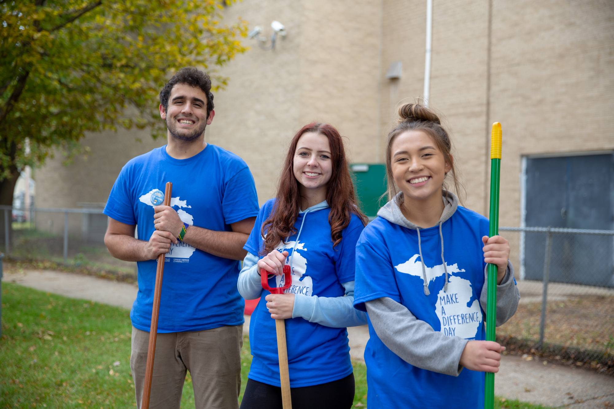 Three students holding gardening tools on Make a Difference Day